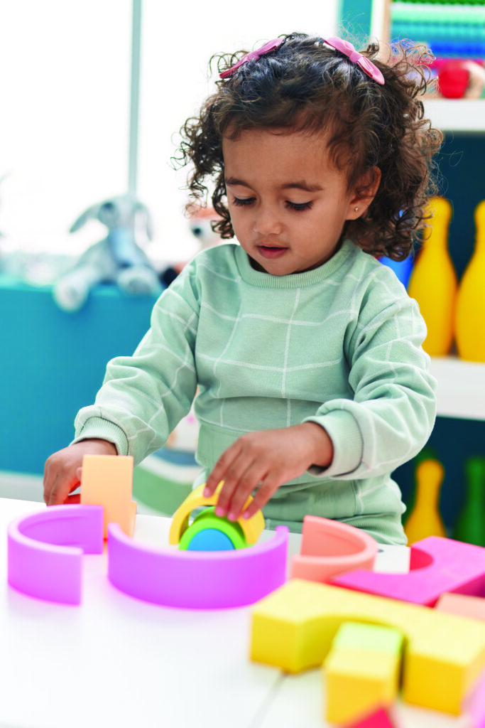 Adorable hispanic girl playing with construction blocks standing at kindergarten