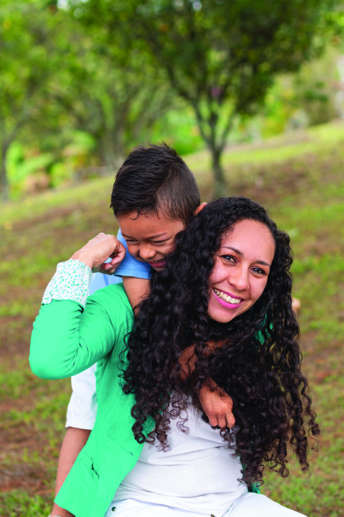 Vertical photo of portrait of happy woman carrying her smiling child on her back while playing